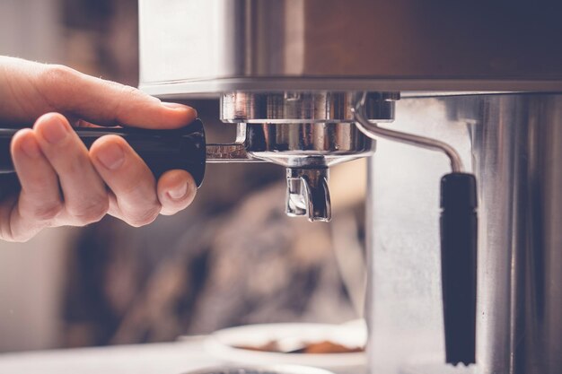 Photo close up of barista holding handle of portafilter holder while putting it into coffee machine