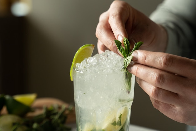 Close up bartender prepares a mojito cocktail at the bar a man decorates a mojito cocktail with mint and lime