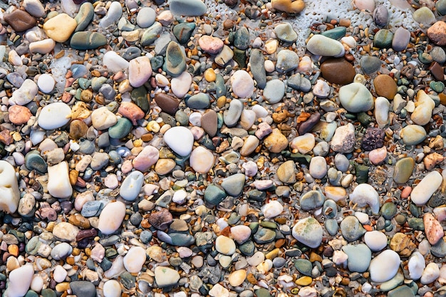 A close up of a beach with colorful pebbles and a black and white stripe on the sand.