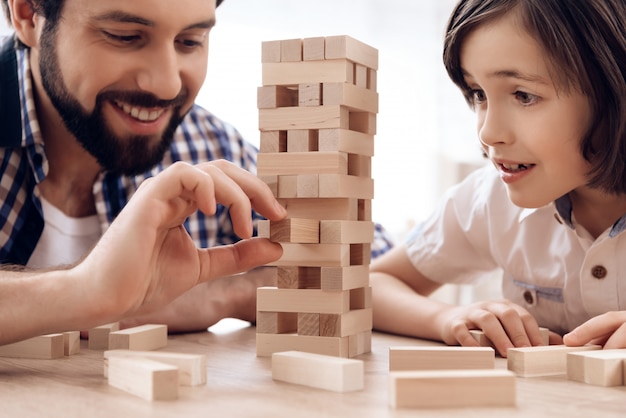 Close up. Bearded father with small son plays Jenga at home.