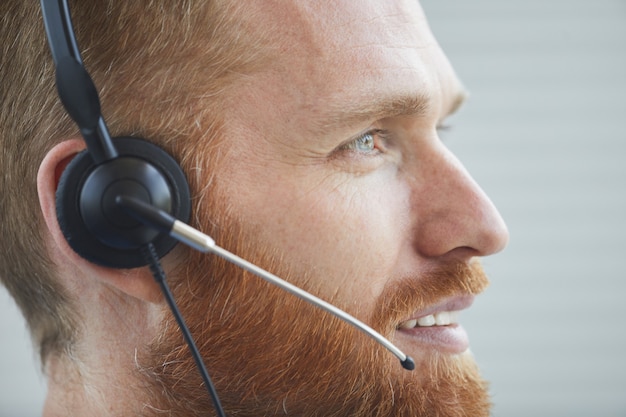 Close-up of bearded man in headphones talking on the phone he working in call center