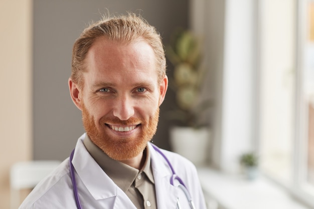 Close-up of bearded successful medical worker in white coat smiling at front