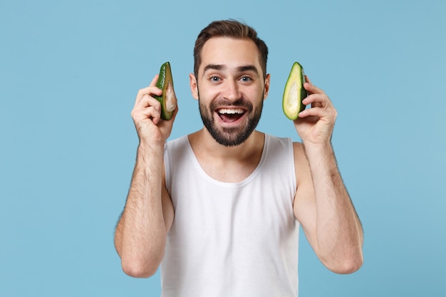 Close up bearded young man 20s years old in white shirt hold half of avocado isolated on blue pastel background, studio portrait. Skin care healthcare cosmetic procedures concept. Mock up copy space.