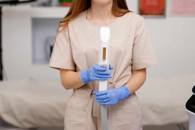 Close up of beautician hand in glove holding ultrasound device for face and skin lifting procedure and hair removal Young woman cosmetologist using modern cosmetology equipment in clinic