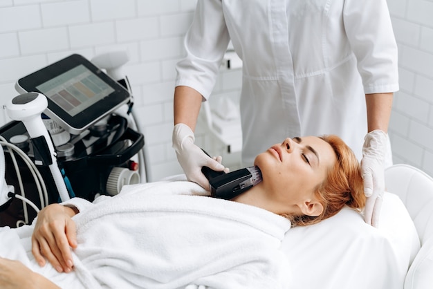 Close up of beautician hand removing hair on lady face with laser epilation machine. Girl laying on the daybed with closed eyes