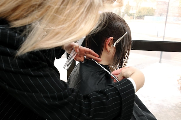 Photo close up of beautician's hand with a comb cutting hair of woman