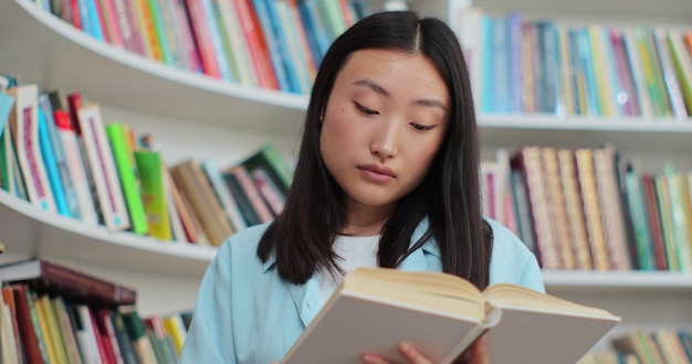 Close up beautiful asian girl in reading book near bookshelf in library of university Self education concept