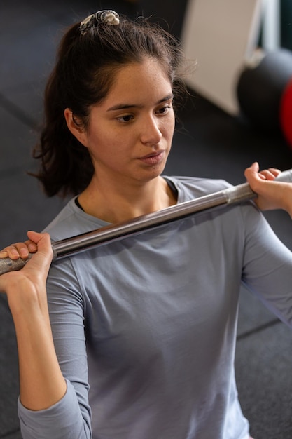 Close up of beautiful sportswoman doing exercises indoors in gym, lifting barbell