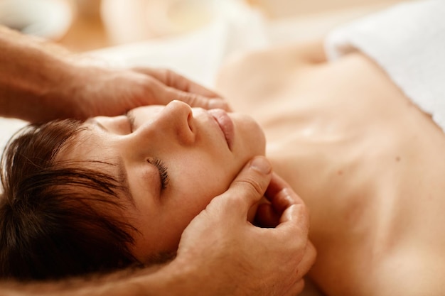 Close up of beautiful young woman enjoying face massage in spa center with eyes closed copy space