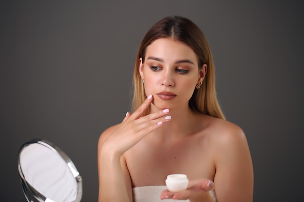 Close up beauty portrait of beautiful half naked woman applying face cream.