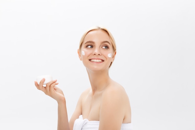 Close up beauty portrait of a laughing beautiful half naked woman applying face cream and looking away