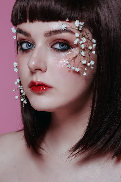 Close up  beauty portrait of young beautiful woman with fresh, smooth, flawless skin, nude makeup with flower on pink wall. Fashion photo