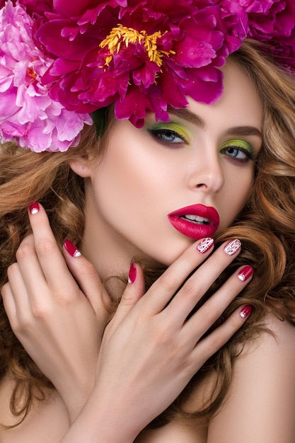 Close-up beauty portrait of young pretty girl with flower wreath in her hair wearing bright pink lipstick and touching her lips. Bright modern summer makeup