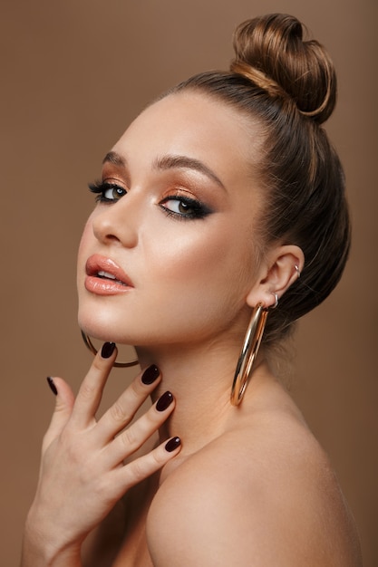 Close up beauty portrait of an young topless woman wearing accessories isolated on brown, posing