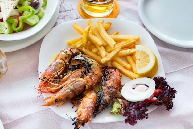 Close up big size grill shrimps with fried potato, vegetables and lemon, lunch time in restaurant.