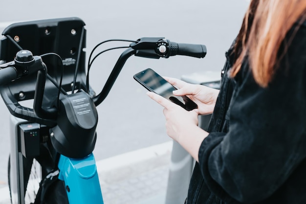 Close up of bike handlebar next to smart phone hold by young hands out of focus rental bikes Writing and reviewing in social media and networks New ways of urban transport in the city or town