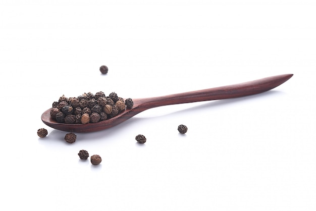 Close up black peper in wooden spoon pile.