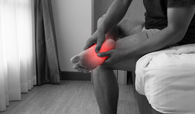 Photo close up black and white blurred image a man sitting in bed and holding feet with plantar ligament pain