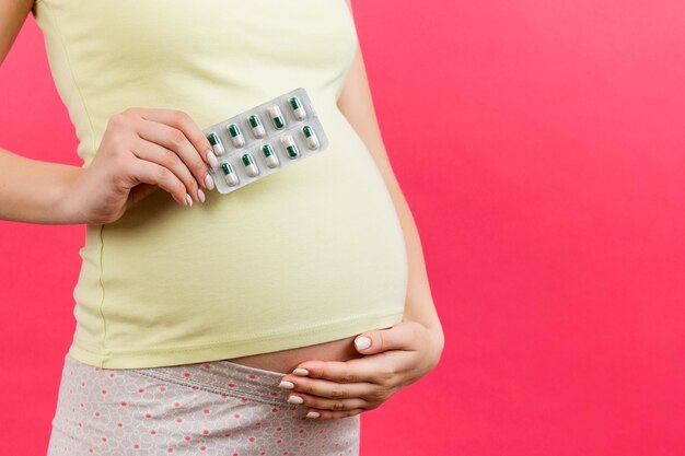 Close up of a blister of pills in pregnant woman's hand against her belly at colorful background with copy space Vitamins during pregnancy concept