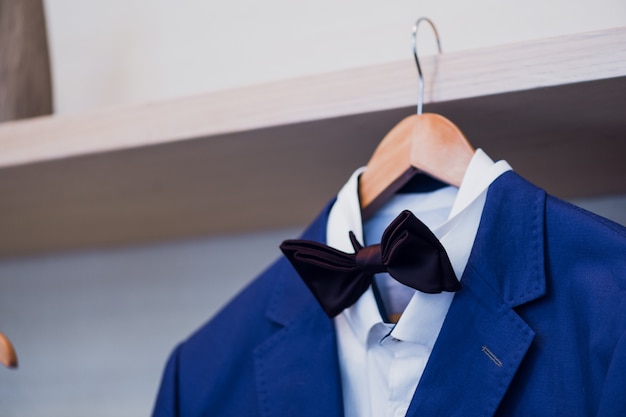 Photo close-up of blue jacket with bow tie on a hanger.