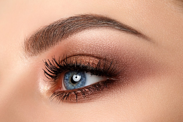 Close up of blue woman eye with beautiful brown with red and orange shades smokey eyes makeup. Modern fashion make up.