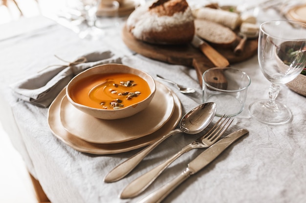 Close up bowl of cream pumpkin soup and fresh bread on wood board on lunch in cozy cafe