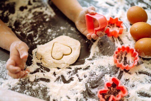 Close up of boy hands carving dough with cookie heart cutters Easter baking preparation