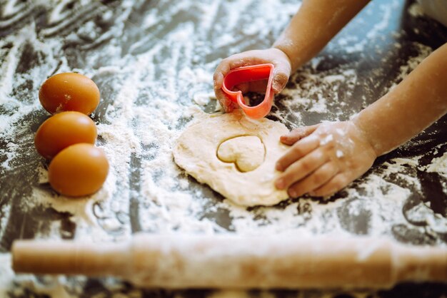 Close up of boy hands carving dough with cookie heart cutters Easter baking preparation