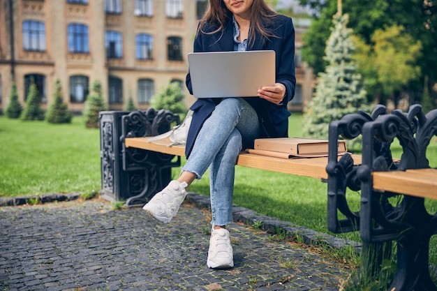 Close up on brunette female sitting on bench with her gadget and enjoying beautiful weather