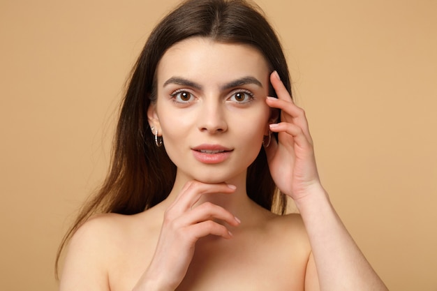 Close up brunette half naked woman 20s with perfect skin, hands on face isolated on beige pastel wall,  portrait. Skin care healthcare cosmetic procedures concept. .