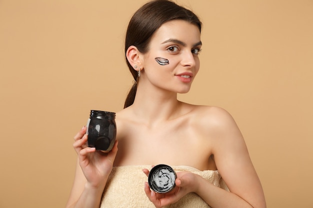 Close up brunette half naked woman with perfect skin, nude make up black mask isolated on beige pastel wall