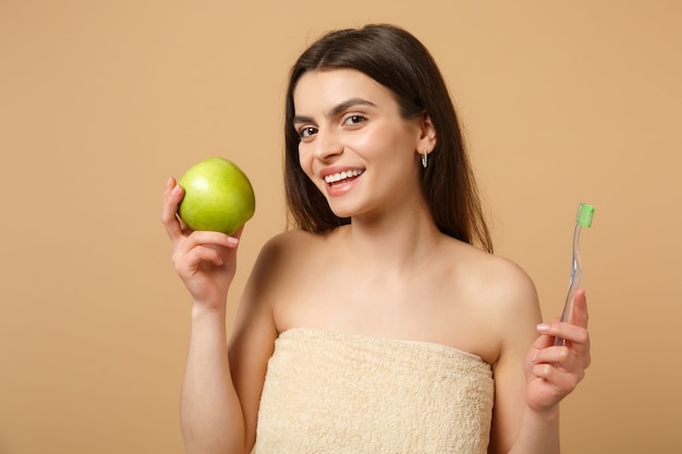 Close up brunette half naked woman with perfect skin, nude make up holds brush isolated on beige pastel wall