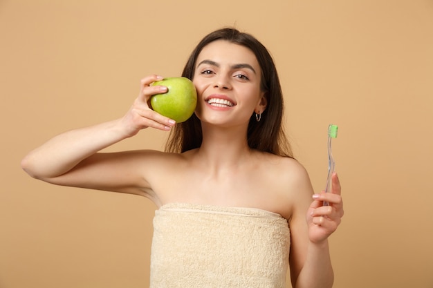 Close up brunette half naked woman with perfect skin, nude make up holds brush isolated on beige pastel wall