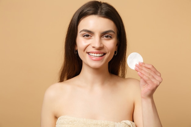 Close up brunette half naked woman with perfect skin, nude make up isolated on beige pastel wall