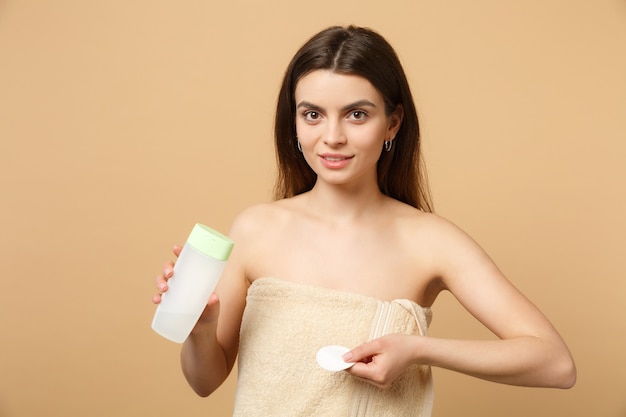 Close up brunette half naked woman with perfect skin, removing nude make up isolated on beige pastel wall