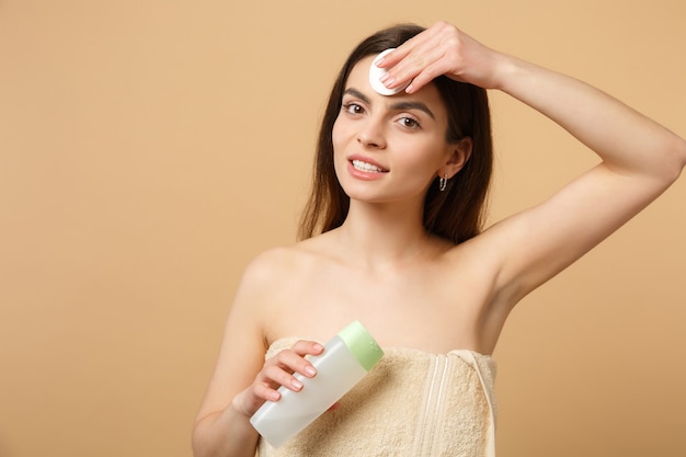 Close up brunette half naked woman with perfect skin, removing nude make up isolated on beige pastel wall