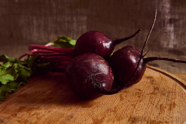 Close-up of a bunch of fresh burgundy wet beetroot with green tops and leaves on a wooden cutting board . Food background of seasonal raw vegetables