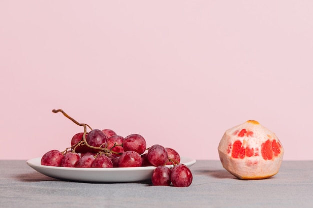 Close-up of a bunch of grapes and a peeled grapefruit on a pink background. Minimalist still life with copy space for your text.