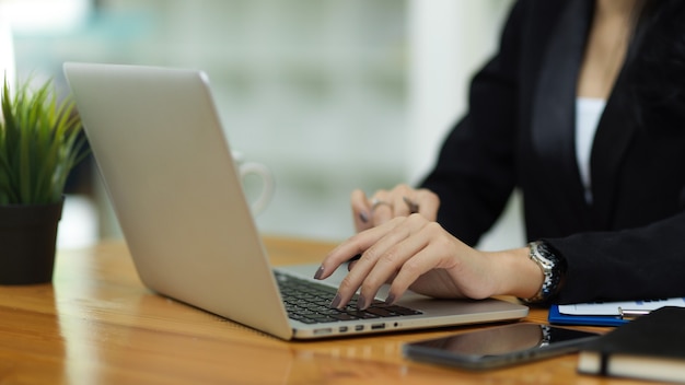 Close up business female in black suit hands typing on laptop keyboard on work space