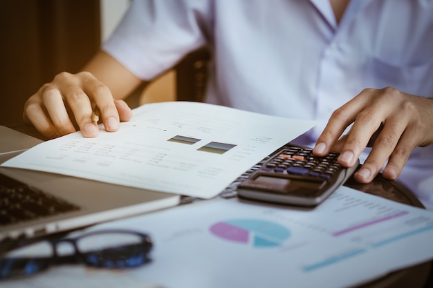 Photo close up business man using calculator and laptop computer for calculating with finance paper, tax, accounting, accountant concept.