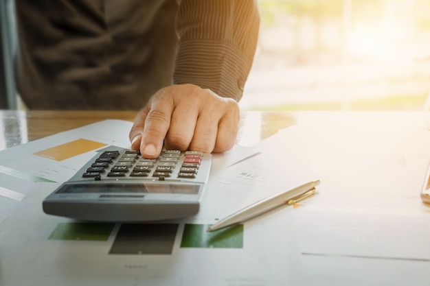 Close up Business man using calculator and laptop computer for calculating with finance paper, tax, accounting, Accountant concept.