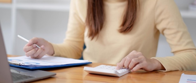 Close up Business woman using calculator and laptop for do math finance on wooden desk in office and business working background tax accounting statistics and analytic research concept