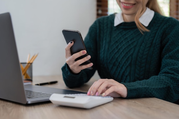 Close up Business woman using calculator and phone for do math finance on wooden desk in office and business working background tax accounting statistics and analytic research concept