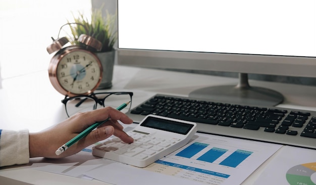 Close up of businessman or accountant hand holding pen working on calculator to calculate business data accountancy document and laptop computer at office business concept