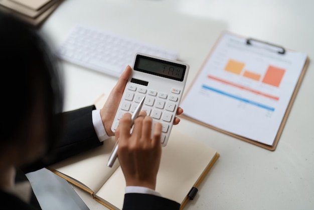 Close up of businessman or accountant hand holding pen working on calculator to calculate business data accountancy document and laptop computer at office business concept