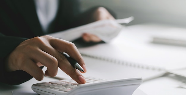 Close up of businessman or accountant hand holding pen working on calculator to calculate business data,finance accounting concept