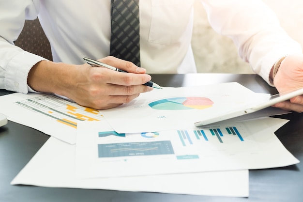 Close up of Businessman analyzing investment charts and using tablet on the desk.