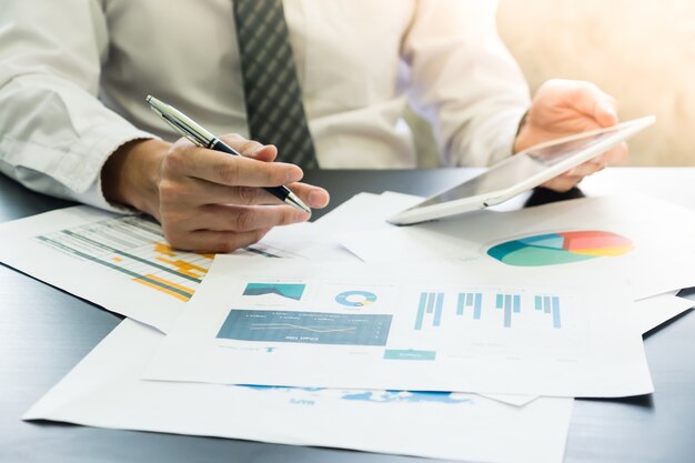 Close up of Businessman analyzing investment charts and using tablet on the desk.