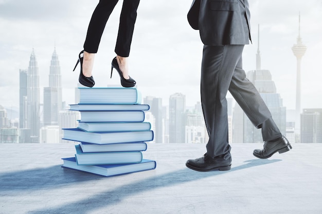 Close up of businessman and businesswoman feets and legs standing on top of stacked books Blurry city wallpaper Education wisdom success growth and teamwork concept