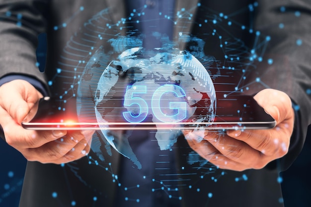 Close up of businessman hand holding digital tablet with globe and 5g hologram on blurry dark bokeh background Telecommunication and internet speed concept Double exposure